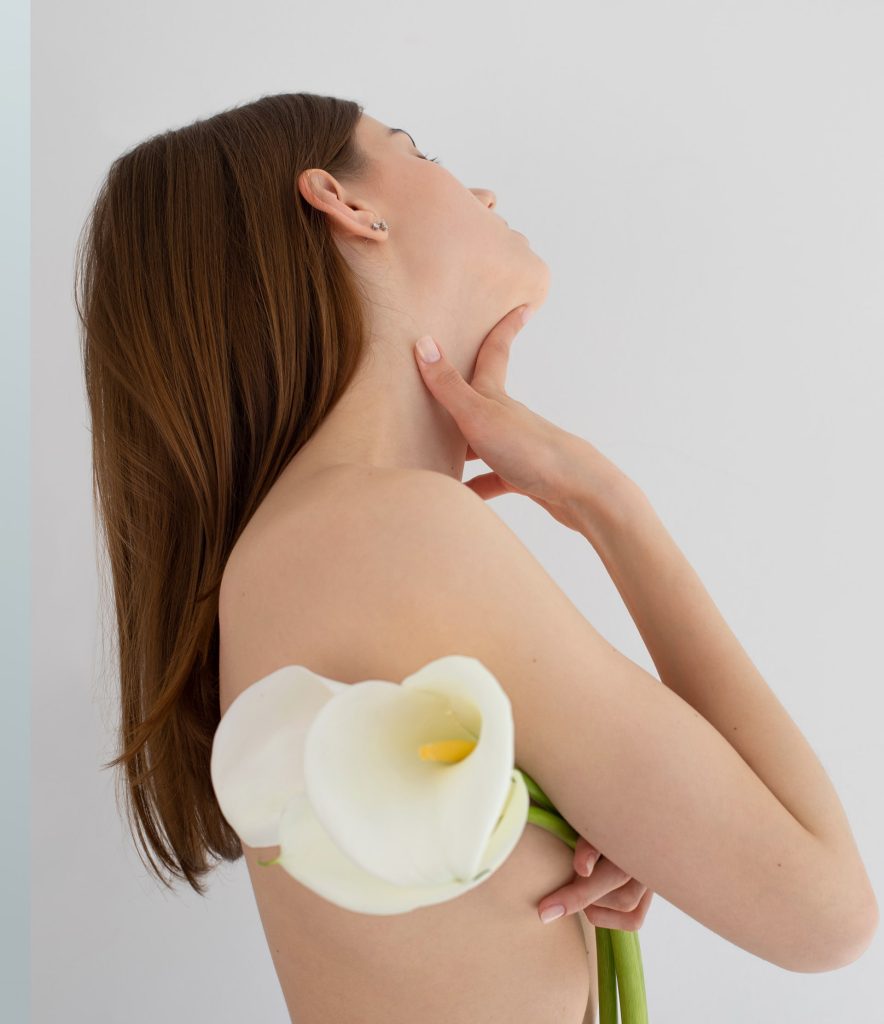 A woman with long brown hair holds white calla lilies across her chest, her head tilted back and one hand touching her neck, embodying a serene sense of wellness against a plain white background.