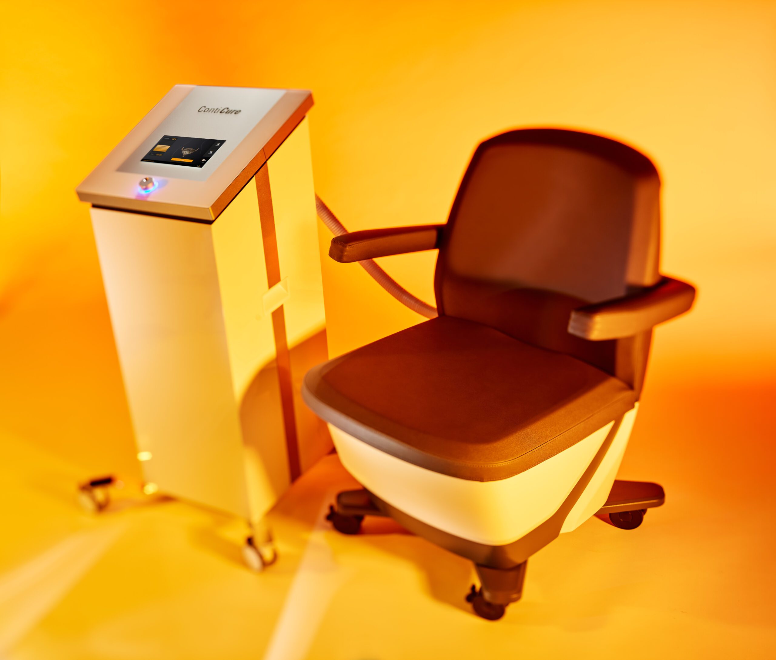 A modern medical chair with armrests is connected to an adjacent control unit on wheels, set against a warm, orange background—an ideal setting for anti-aging treatments at the Institute For Ageless Living.
