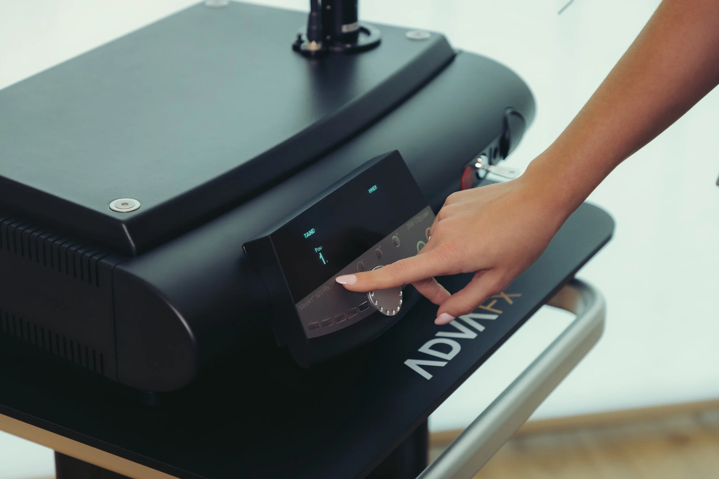 A person's hand adjusts the settings on a touchscreen control panel of a black ADVIMED medical or technical device, supporting wellness and anti-aging therapies at the Institute For Ageless Living.