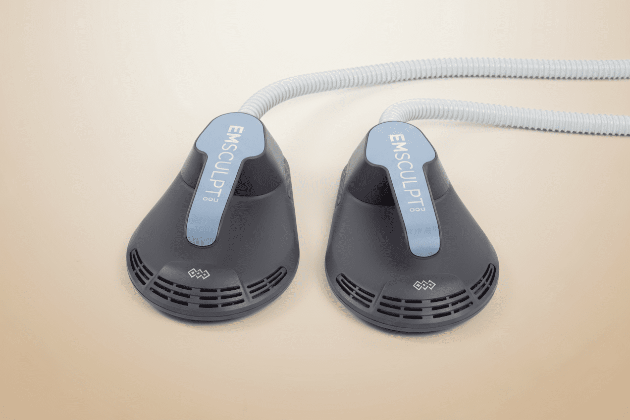 Two gray and blue medical device applicators labeled EMSCULPT, designed for wellness and anti-aging treatments, with flexible white cables attached, placed side by side on a beige surface—an innovative offering from the Institute For Ageless Living.