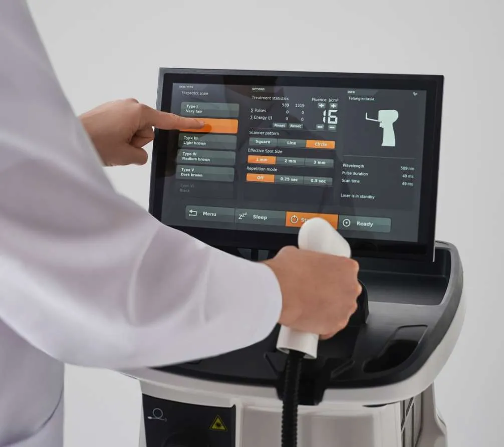 A person in a white coat operates a medical device, adjusting settings on a touchscreen while holding a handheld applicator attached to the machine. The screen displays various adjustable treatment options designed to support wellness and anti-aging therapies at the Institute For Ageless Living.