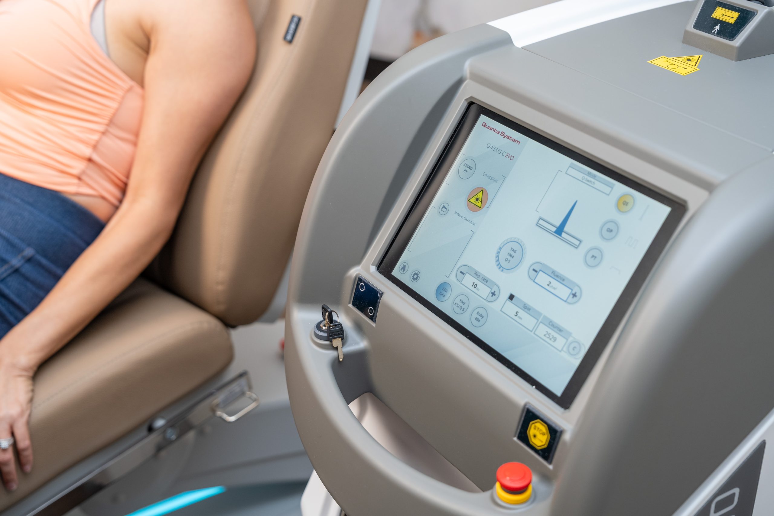 A person sits in a medical chair next to a machine with a touchscreen displaying controls and settings, likely for a wellness or anti-aging procedure at the Institute For Ageless Living.