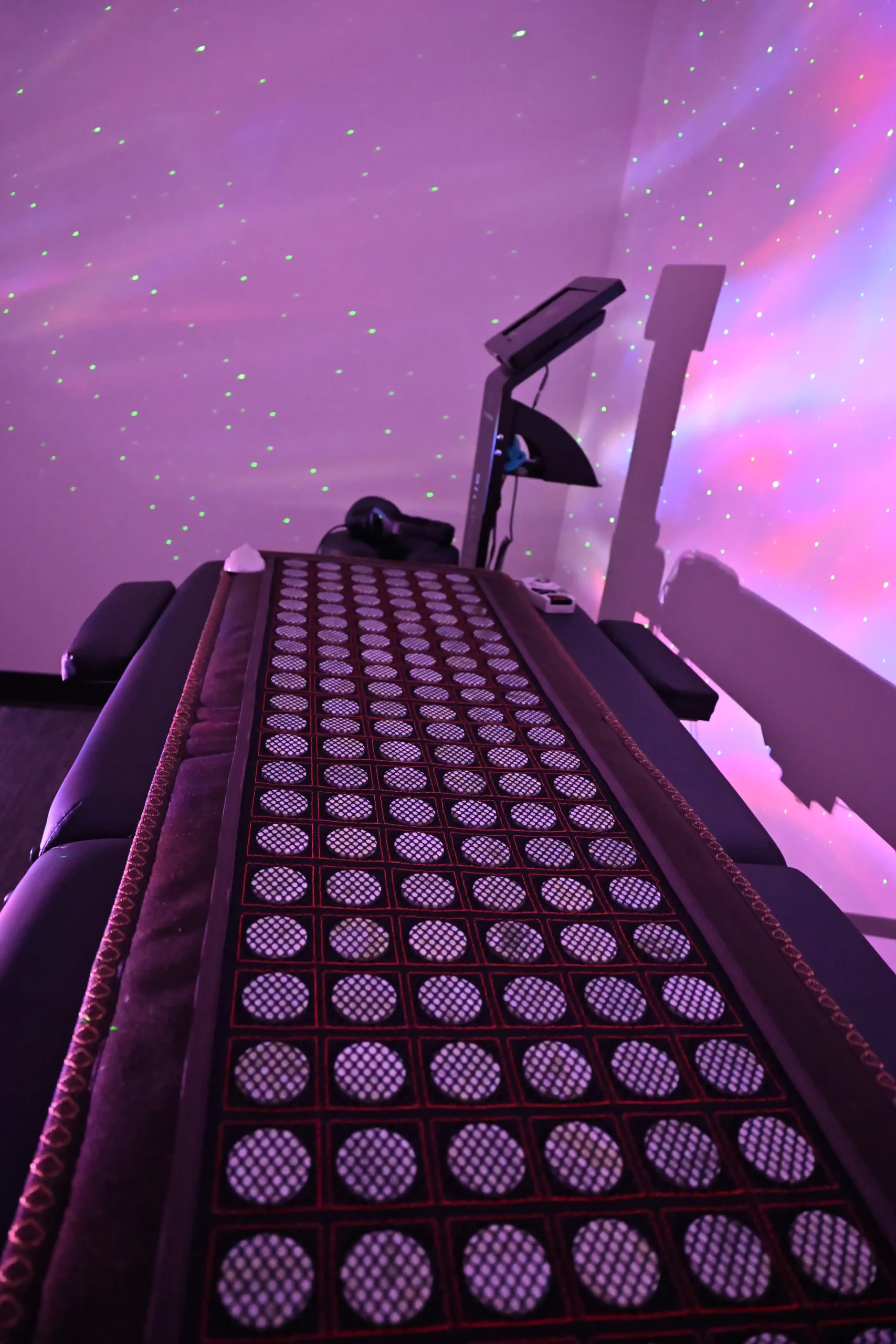 Massage table with a patterned mat in a softly lit room, featuring purple and pink lights with green spots on the wall, creating a calming, spa-like atmosphere designed to promote wellness and support anti-aging treatments at the Institute For Ageless Living.