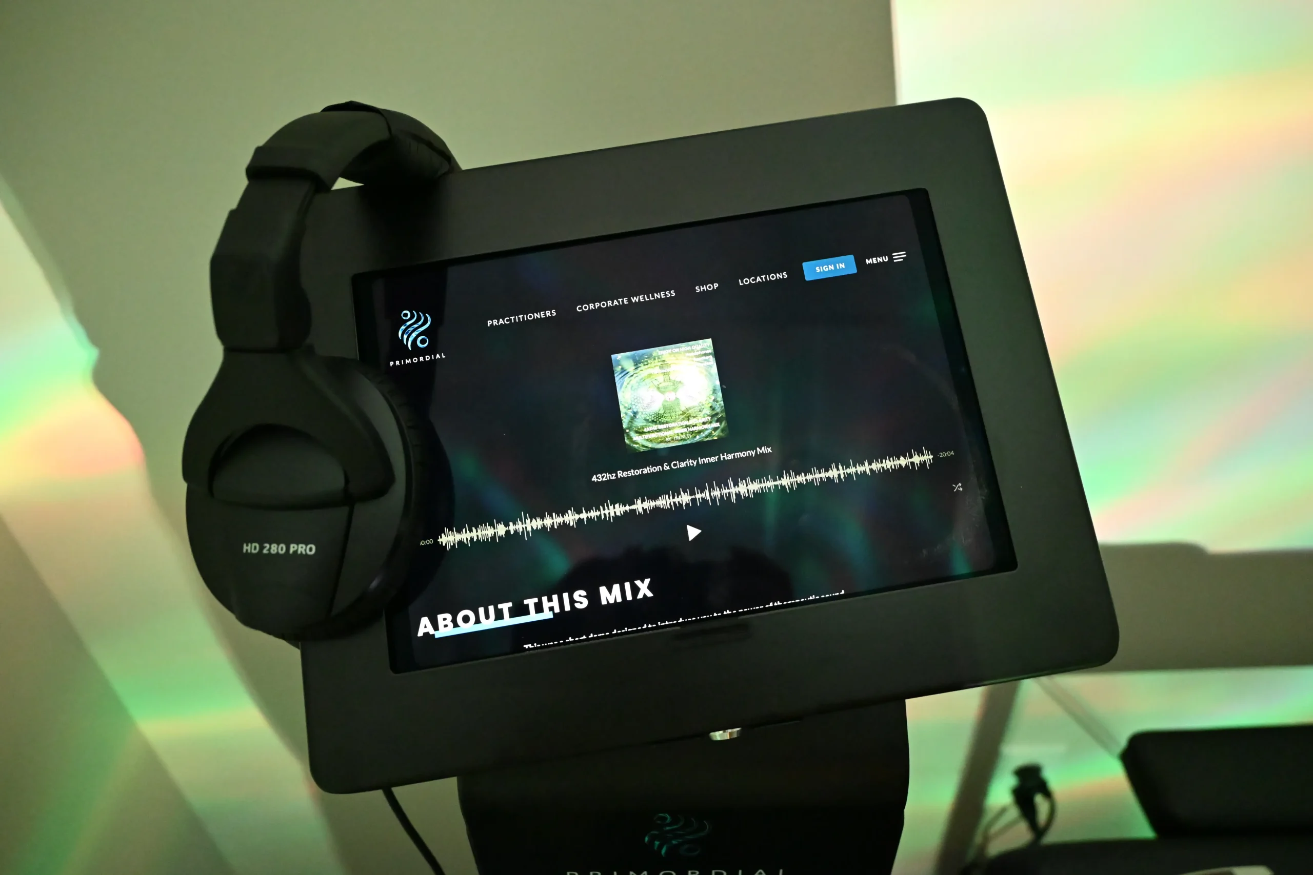 A pair of black headphones rests on a display screen showing music playback with album art, waveform, and text about the mix, evoking a sense of wellness inspired by the Institute For Ageless Living.