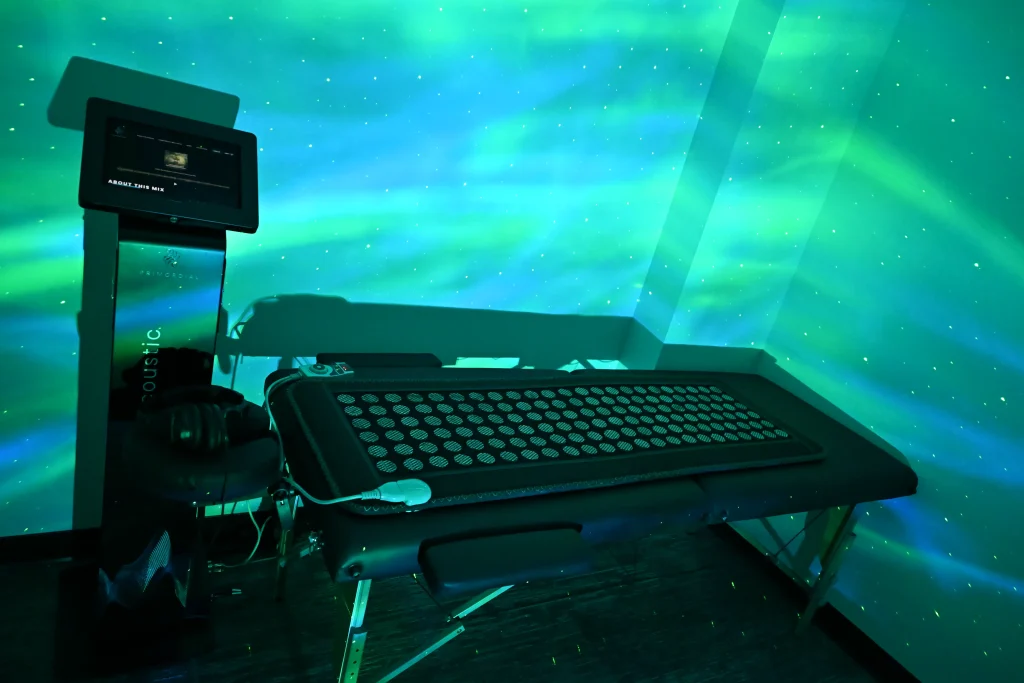 A dark room with green and blue lights, featuring a massage table with headphones and a control screen on a stand nearby—creating an atmosphere where wellness meets innovation at the Institute For Ageless Living.