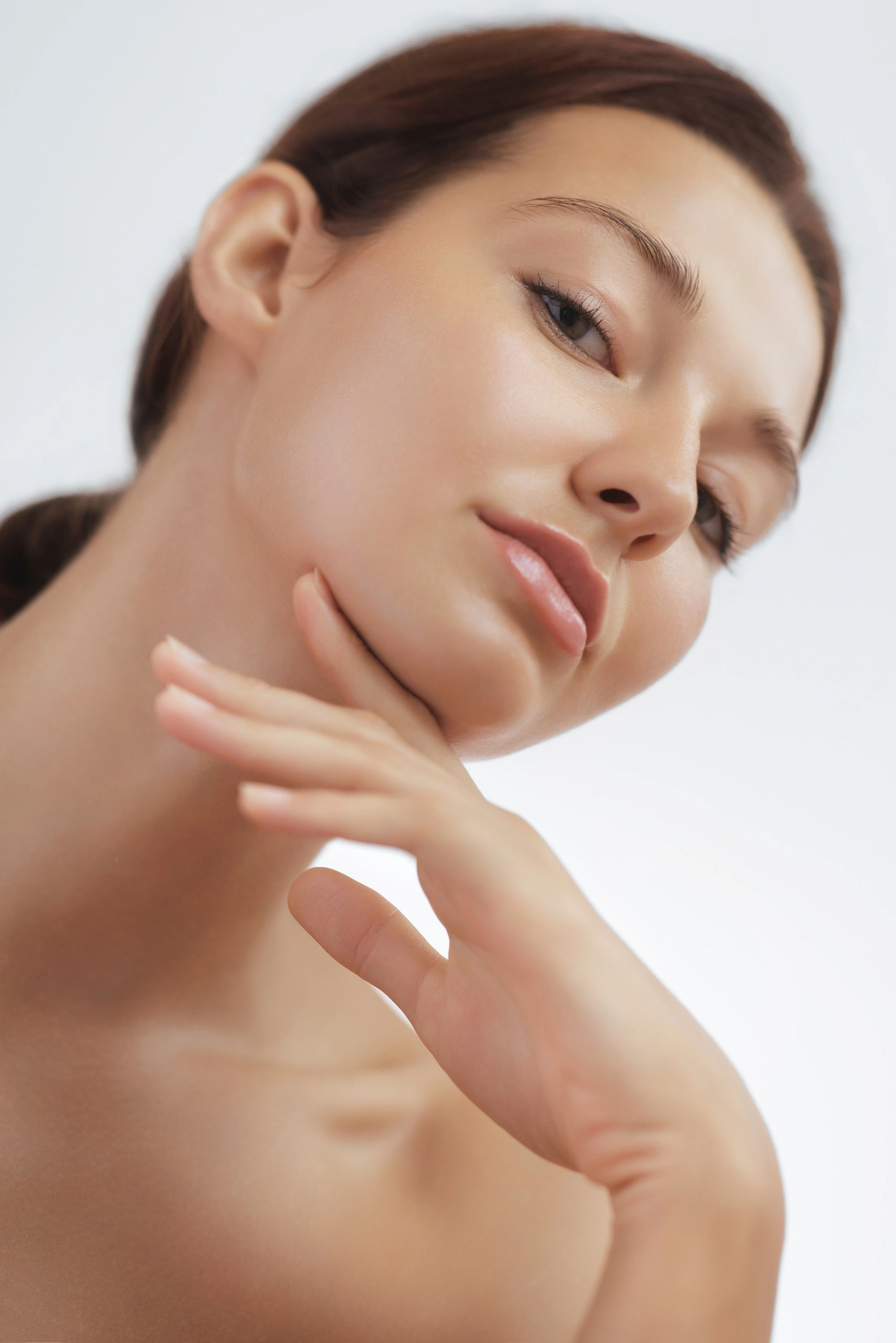 A woman with clear skin tilts her head back slightly and gently touches her chin with her hand, posing against a light background.